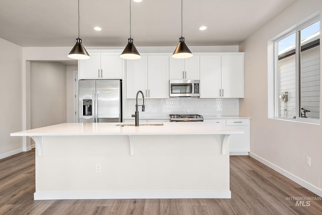 kitchen with appliances with stainless steel finishes, a sink, hanging light fixtures, and an island with sink