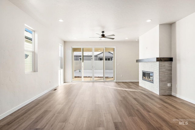 unfurnished living room featuring ceiling fan, a glass covered fireplace, wood finished floors, and baseboards