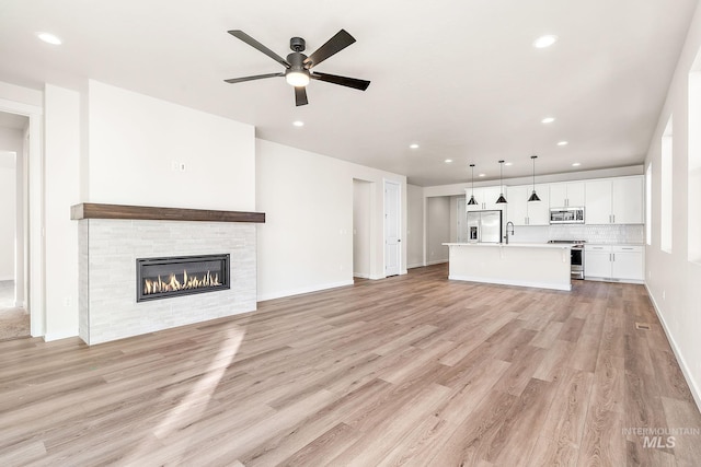 unfurnished living room featuring ceiling fan, a fireplace, light wood-style flooring, and recessed lighting