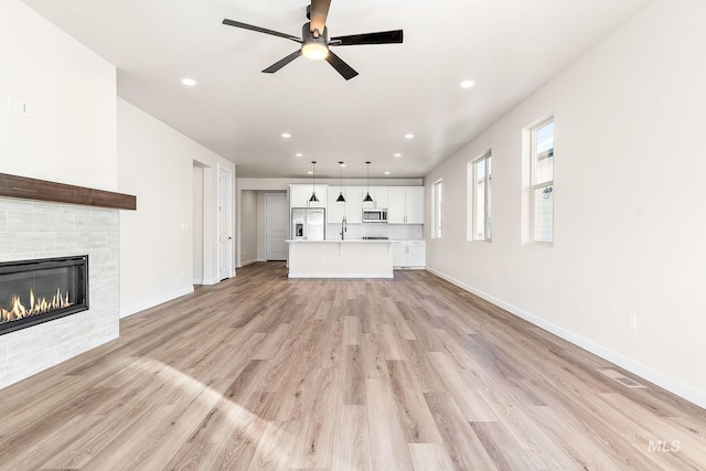 unfurnished living room featuring recessed lighting, a sink, baseboards, light wood-style floors, and a glass covered fireplace