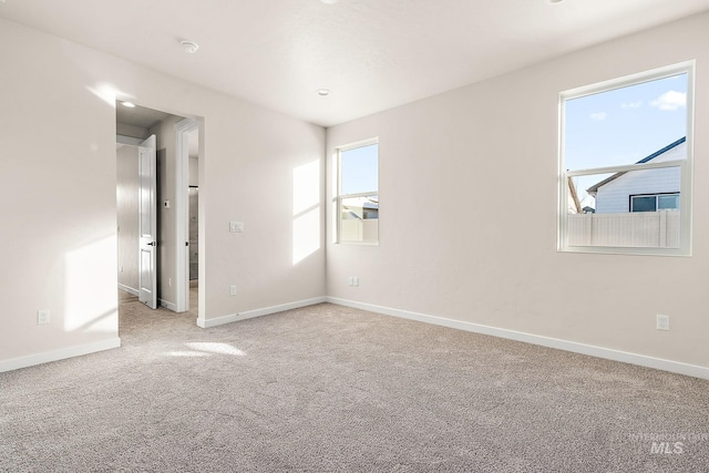 empty room featuring baseboards, a healthy amount of sunlight, and light colored carpet