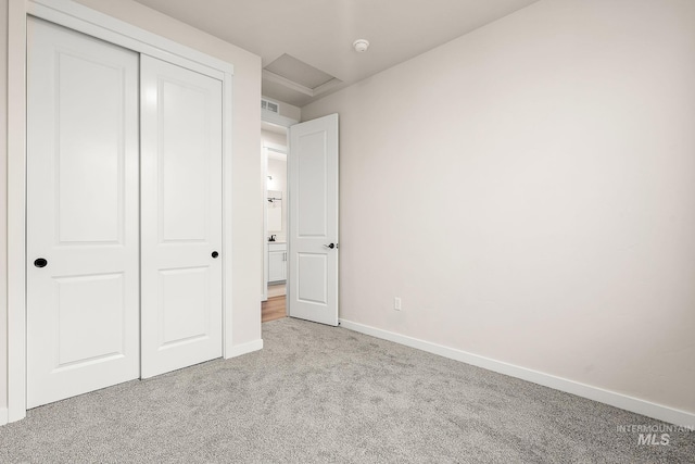 unfurnished bedroom featuring light carpet, visible vents, baseboards, a closet, and attic access