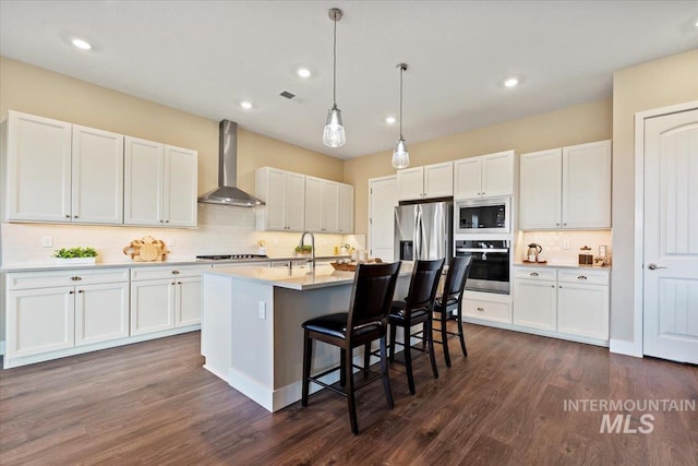 kitchen featuring white cabinetry, appliances with stainless steel finishes, a breakfast bar area, and wall chimney range hood