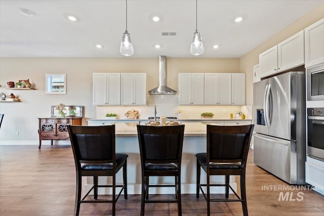 kitchen with tasteful backsplash, appliances with stainless steel finishes, wood finished floors, and wall chimney range hood