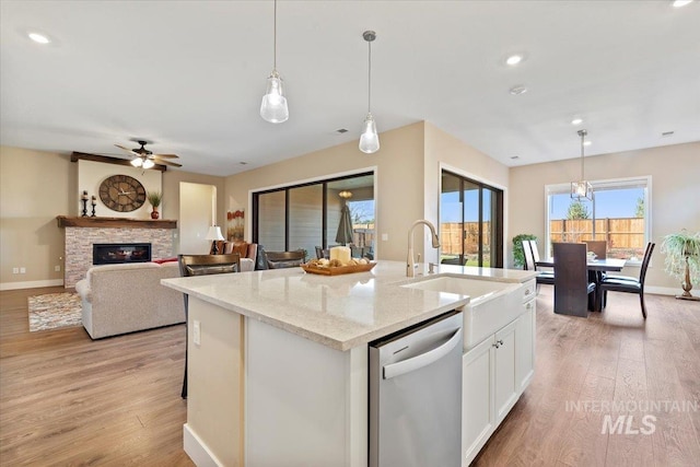 kitchen featuring a sink, dishwasher, a stone fireplace, and light wood finished floors