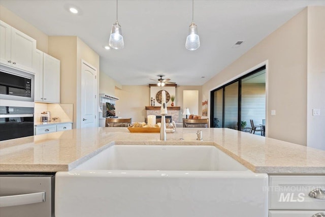 kitchen with black oven, ceiling fan, light stone countertops, built in microwave, and a fireplace