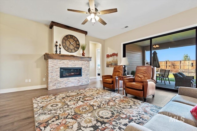 living area featuring wood finished floors, visible vents, baseboards, a ceiling fan, and a stone fireplace