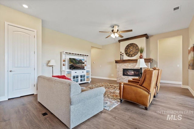 living area with wood finished floors, visible vents, baseboards, ceiling fan, and a stone fireplace