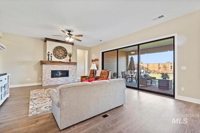 living room featuring a fireplace, a ceiling fan, baseboards, and wood finished floors