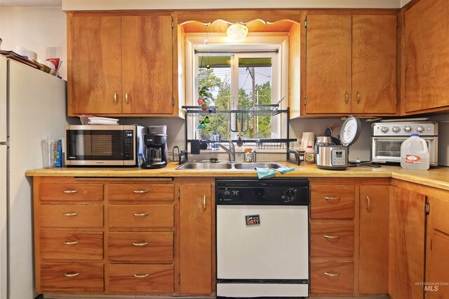 kitchen featuring a sink, light countertops, white appliances, and brown cabinets