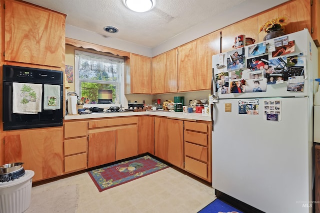 kitchen with oven, light countertops, freestanding refrigerator, a textured ceiling, and stovetop