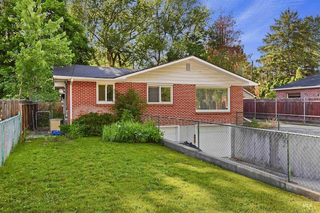 back of house with brick siding, a fenced backyard, an attached garage, and a lawn