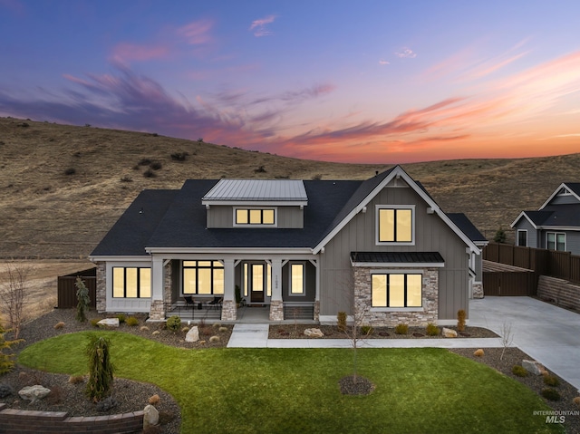 view of front of property featuring stone siding, a porch, concrete driveway, and fence