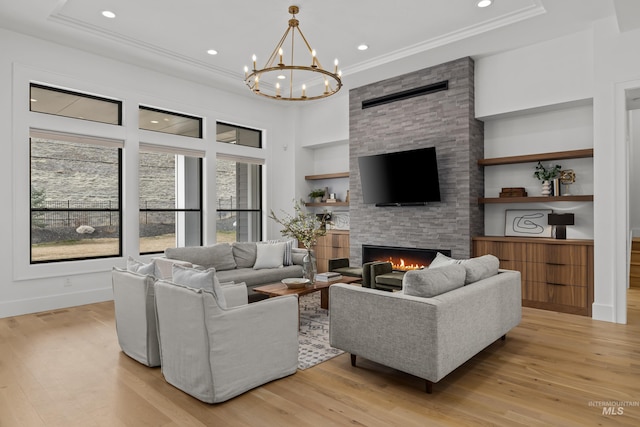 living room with a stone fireplace, built in shelves, light wood finished floors, and a chandelier