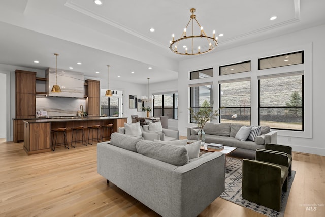 living room with a tray ceiling, recessed lighting, an inviting chandelier, crown molding, and light wood finished floors