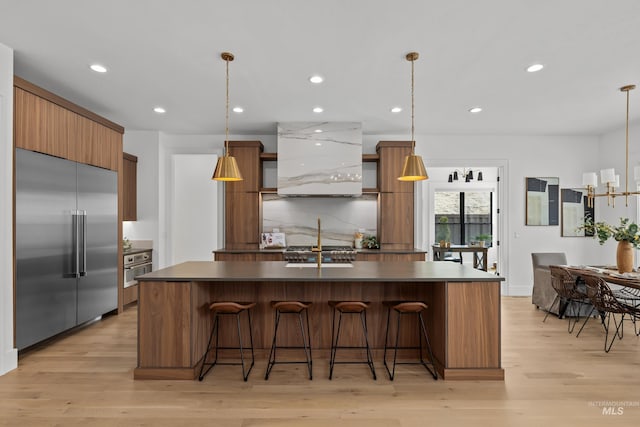 kitchen with a breakfast bar, light wood-style flooring, tasteful backsplash, dark countertops, and built in fridge