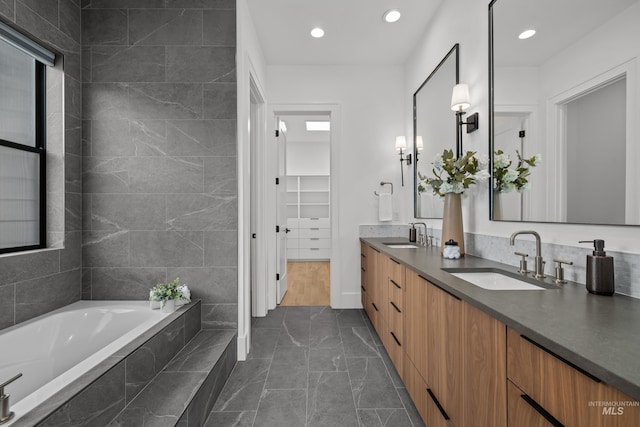 bathroom with double vanity, a walk in closet, a garden tub, and a sink