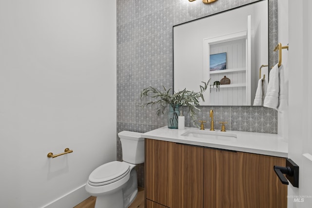 half bathroom with vanity, toilet, baseboards, and backsplash