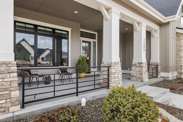 property entrance with stone siding, a porch, and roof with shingles