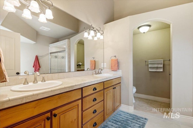 bathroom featuring tile patterned floors, toilet, vanity, a shower with door, and a notable chandelier