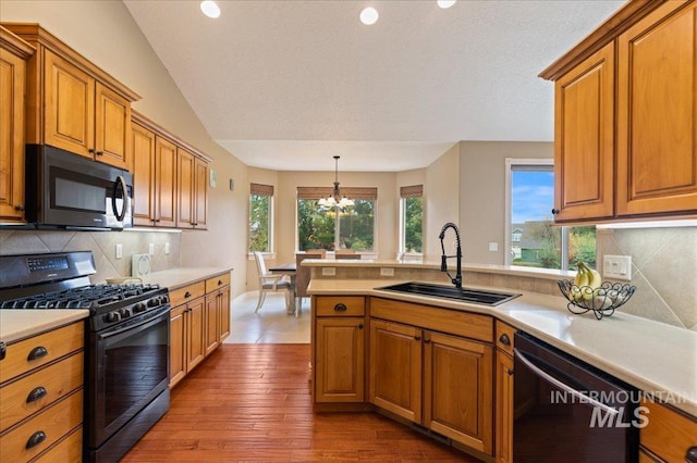 kitchen with lofted ceiling, sink, hanging light fixtures, black appliances, and a healthy amount of sunlight