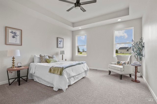 bedroom featuring a raised ceiling, multiple windows, carpet flooring, and ceiling fan