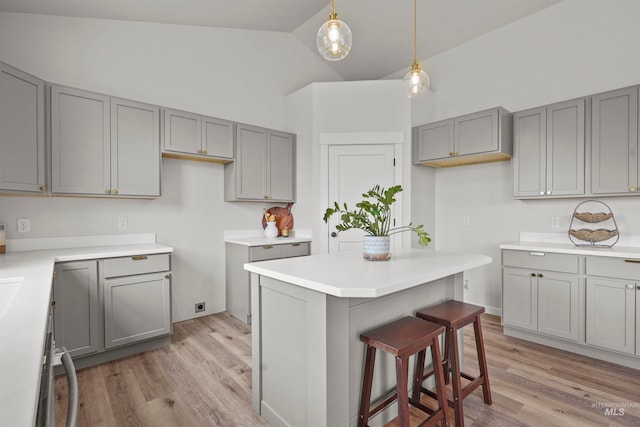 kitchen with high vaulted ceiling, decorative light fixtures, gray cabinets, a center island, and light wood-type flooring