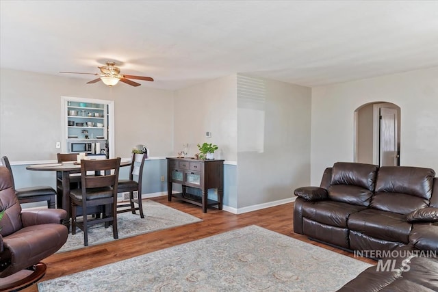 living room with baseboards, wood finished floors, arched walkways, and ceiling fan