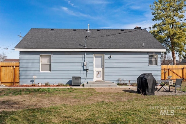 back of property with a lawn, cooling unit, a shingled roof, and fence