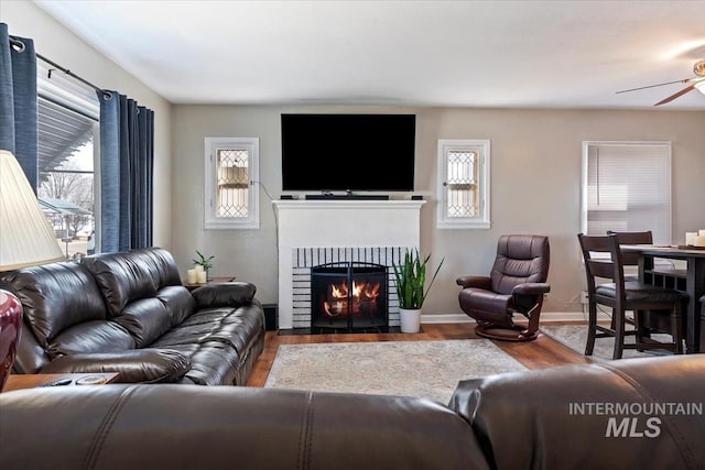 living area featuring a fireplace with flush hearth, baseboards, a ceiling fan, and wood finished floors