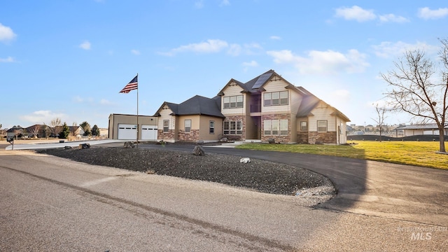 view of front of home with stone siding, a front yard, an attached garage, and driveway