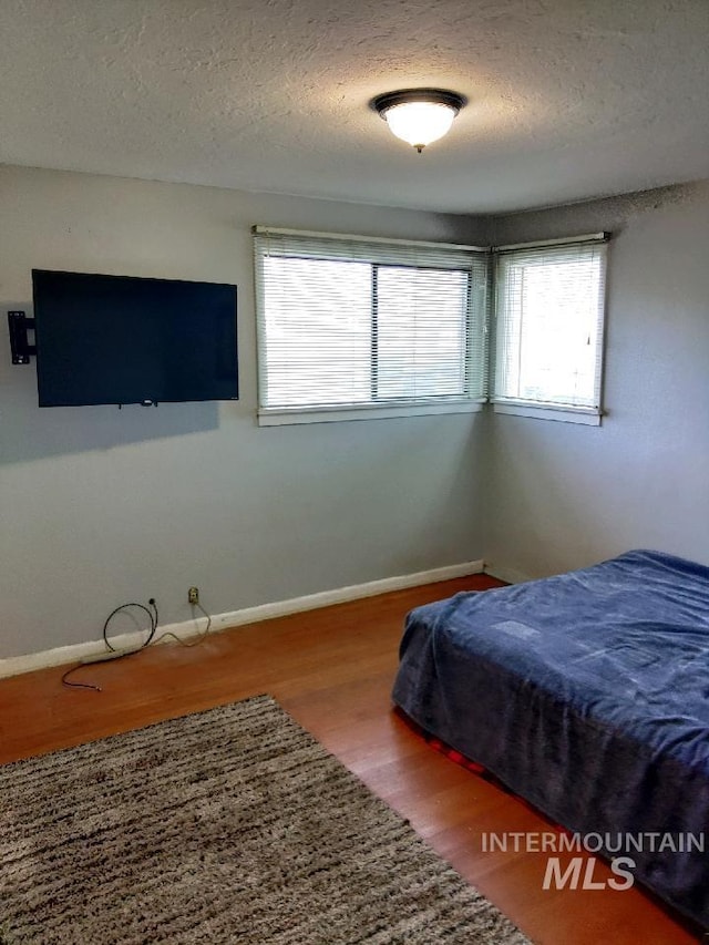 bedroom with multiple windows, a textured ceiling, and hardwood / wood-style floors