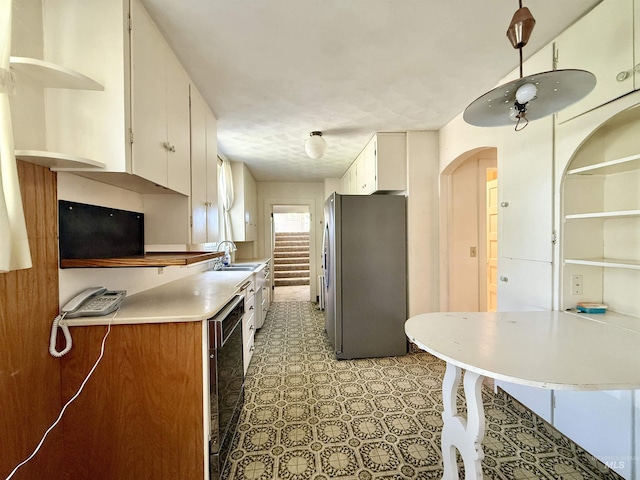 kitchen featuring freestanding refrigerator, open shelves, a sink, and white cabinets