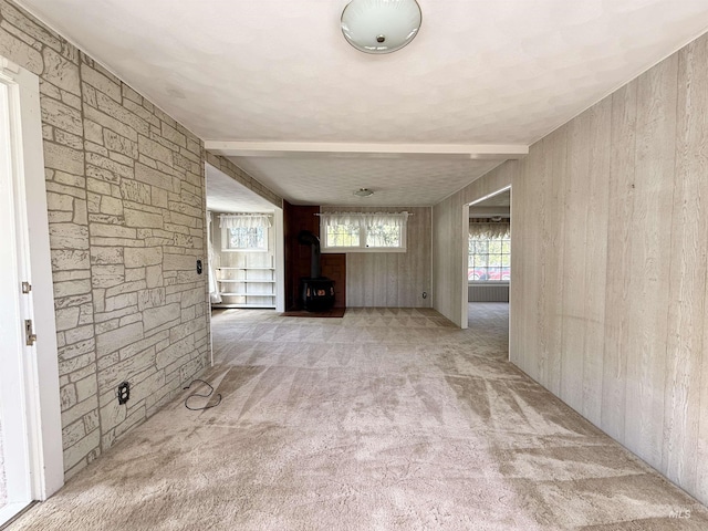 unfurnished living room featuring a wood stove, carpet floors, and wooden walls