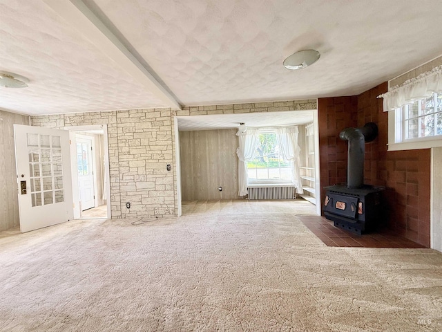 unfurnished living room with carpet, a wood stove, and a textured ceiling