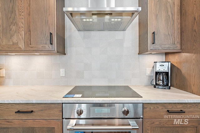 kitchen featuring wall chimney exhaust hood, stainless steel oven, black electric stovetop, light stone countertops, and decorative backsplash