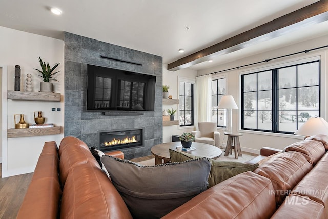 living room featuring a tiled fireplace, hardwood / wood-style floors, and beamed ceiling