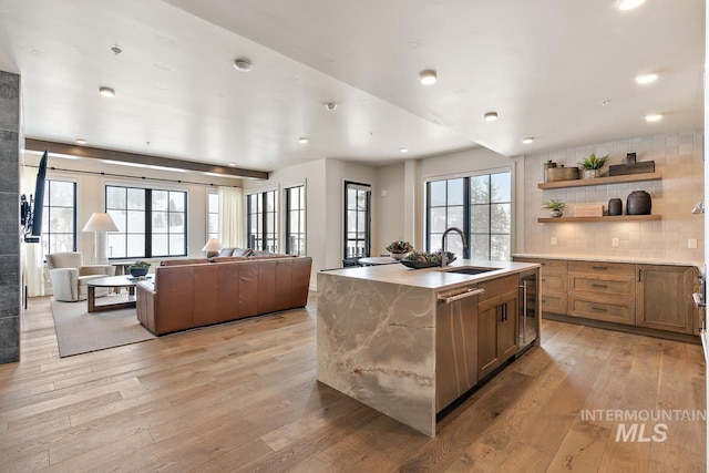 kitchen featuring sink, dishwasher, light hardwood / wood-style floors, a center island with sink, and decorative backsplash