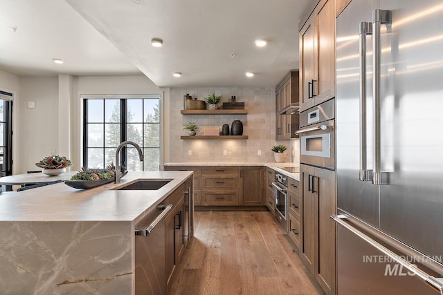 kitchen featuring sink, light hardwood / wood-style flooring, appliances with stainless steel finishes, a kitchen island with sink, and tasteful backsplash