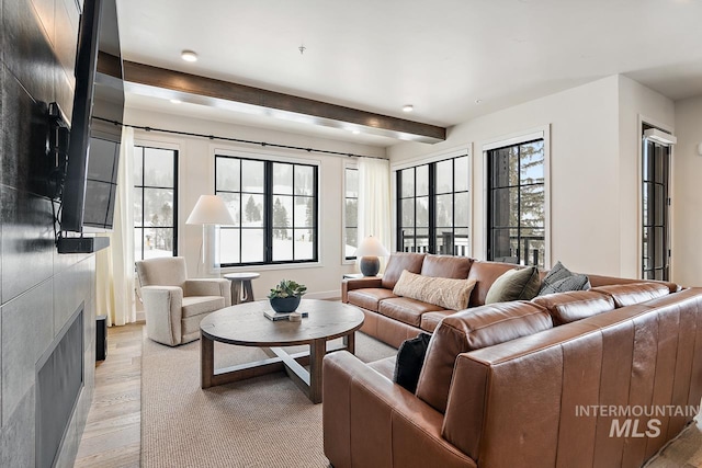 living room with beamed ceiling, plenty of natural light, a fireplace, and light wood-type flooring