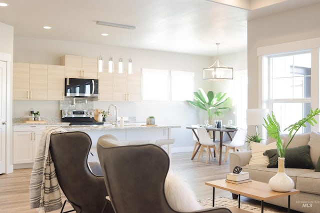 kitchen with appliances with stainless steel finishes, light stone countertops, white cabinetry, hanging light fixtures, and a breakfast bar area