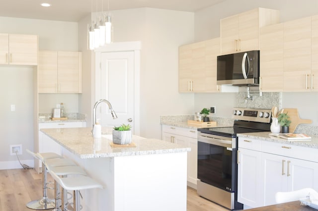 kitchen with decorative light fixtures, white cabinets, appliances with stainless steel finishes, and an island with sink