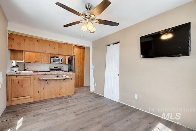 201 W A St, Vale, OR 97918 - kitchen featuring stainless steel appliances, light wood finished floors, a peninsula, a ceiling fan, and a kitchen breakfast bar