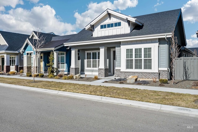 craftsman house featuring a shingled roof, fence, board and batten siding, and brick siding