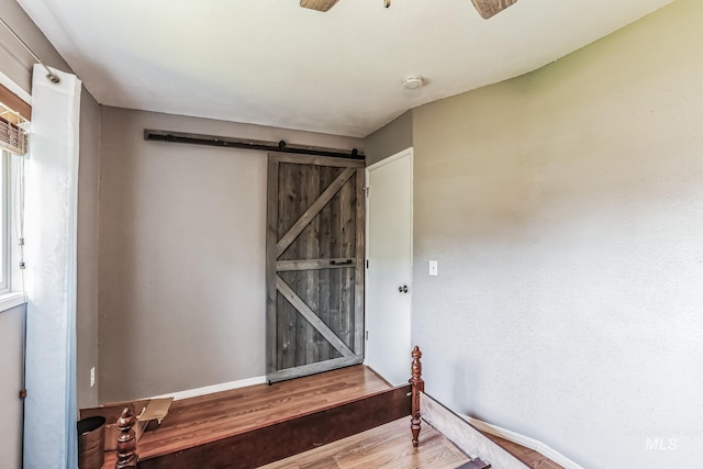 interior space with a barn door, ceiling fan, and hardwood / wood-style flooring