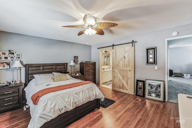 bedroom featuring ceiling fan, a barn door, ensuite bathroom, and dark wood-type flooring