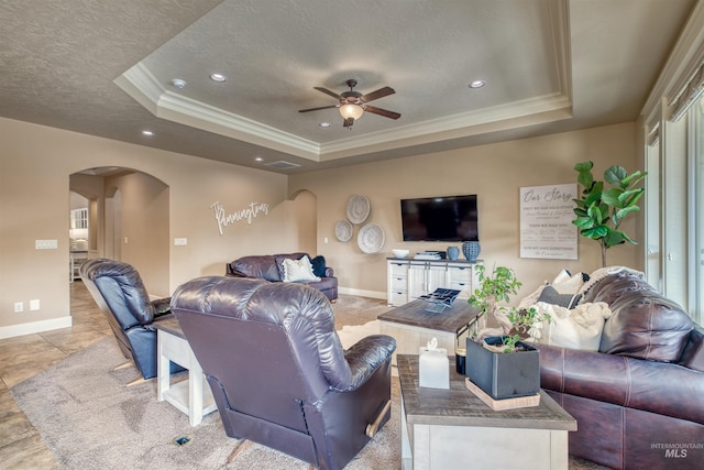 living room with ceiling fan, ornamental molding, a textured ceiling, and a tray ceiling