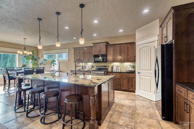 kitchen with a spacious island, black appliances, dark stone counters, a kitchen breakfast bar, and hanging light fixtures