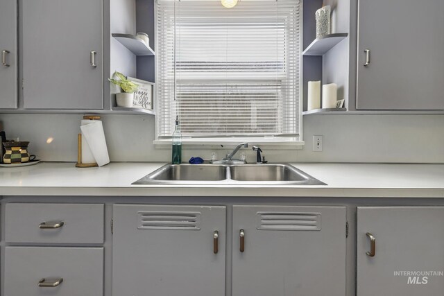 kitchen featuring open shelves, light countertops, gray cabinets, and a sink