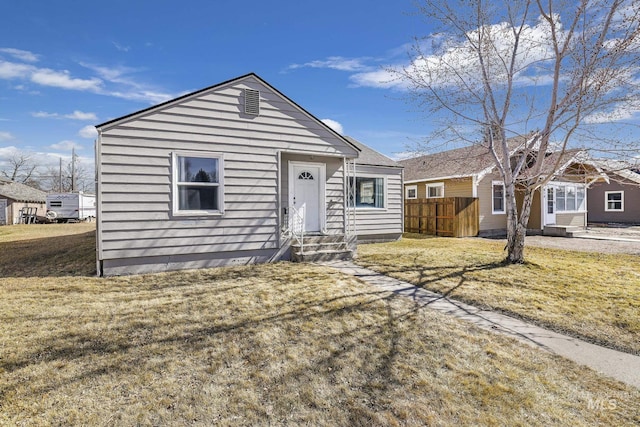 view of front of house with entry steps, a front yard, and fence